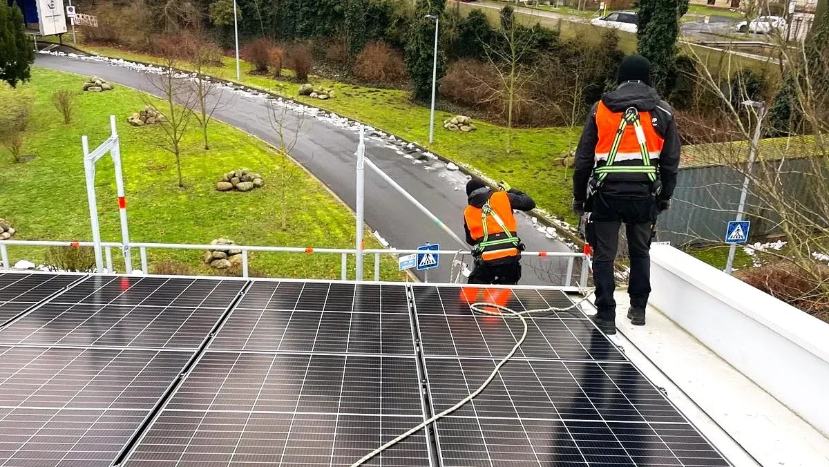 Zwei Monteure mit Sicherheitsgurten installieren eine Photovoltaikanlage auf einem Flachdach